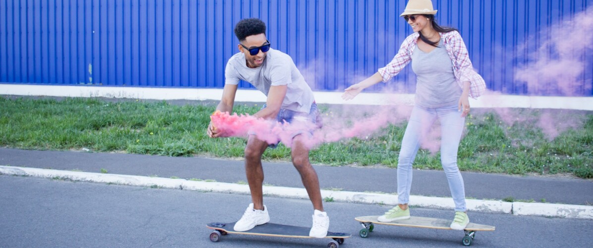 Couple Riding Skateboards and Enjoying The Neighborhood With A Pink Smoke Bomb at Our Apartments Near Assembly Row